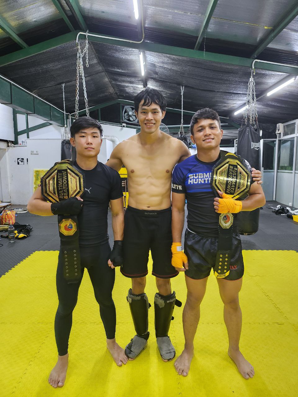 Two Wasp MMA fighters holding their title belts alongside Head Coach Josh